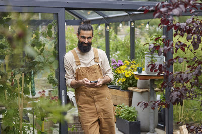 Man using cell phone in front of greenhouse