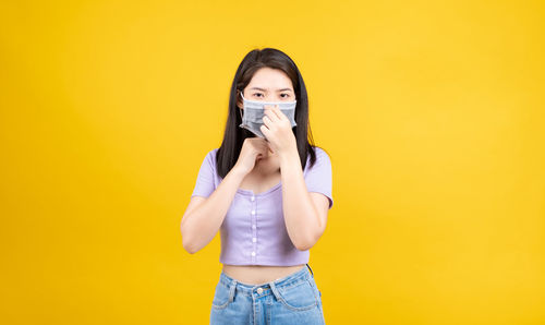 Full length portrait of woman standing against yellow background