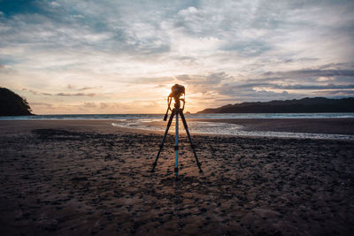 Tripod at beach against sky during sunset