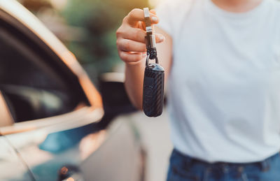 Midsection of man holding camera while standing by car