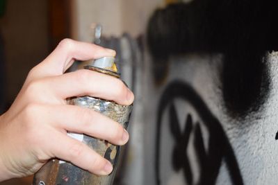 Cropped hand of man making graffiti with spray paint on wall