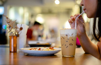 Midsection of woman drinking glass on table at restaurant