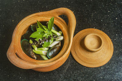 Fresh and raw mussels with basil and lemongrass in clay pot for seafood preparation.