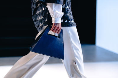 Fashion details of white pants and small blue handbag in a woman's hand. elegant clothing