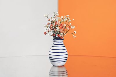 Flower vase against white and orange wall on table