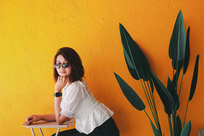 Young woman standing against yellow wall