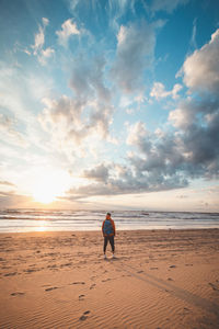 Rear view of woman walking at beach against sky