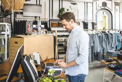 Side view of salesman using laptop while standing in clothing store