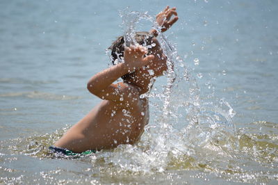 Side view of shirtless boy splashing water in lake