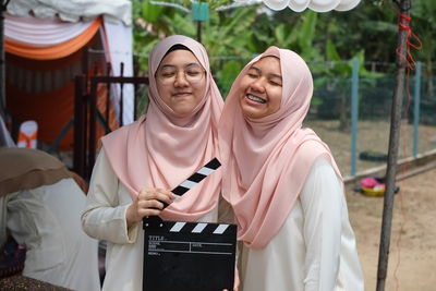 Smiling woman wearing hijab with closed eyes holding film slate