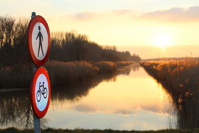 Reflection of trees in calm lake with signboard in foreground