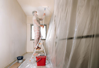 Man working with paint roller on ceiling in kitchen at home 