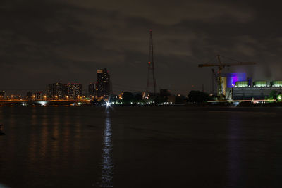 Illuminated buildings by river against sky at night