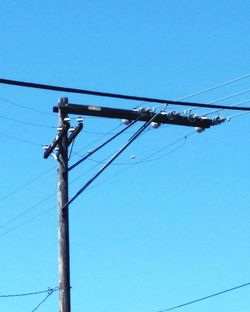 Low angle view of electricity pylon against blue sky