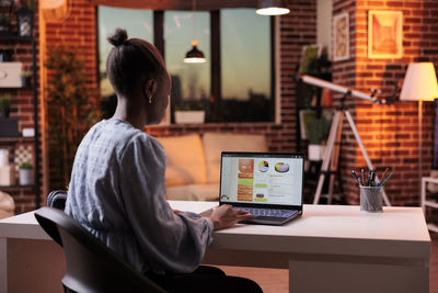 Side view of woman using laptop while sitting on chair