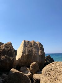 Rocks by sea against clear blue sky