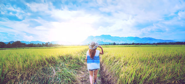 Rear view of woman walking on field against sky