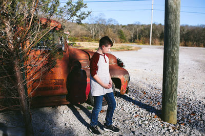 Full length of boy standing by car on field