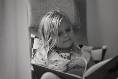 Cute girl reading book while sitting at home