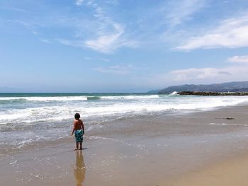 Rear view of man standing at beach against sky