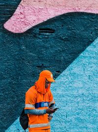 Man holding umbrella standing against orange wall