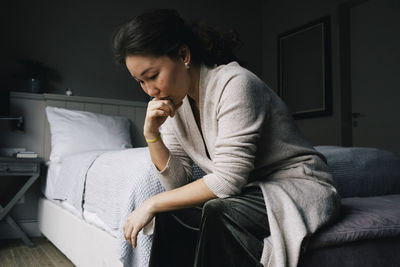 Sad woman sitting with hand on chin in bedroom at home