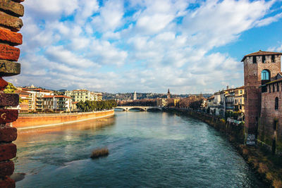 Arch bridge over river amidst buildings in city against sky