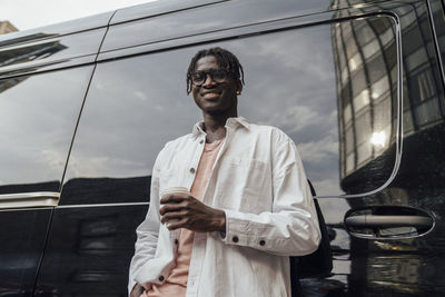 Smiling young man with disposable coffee cup standing in front of van