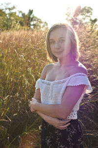 Portrait of smiling young woman standing against plants on field