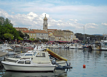 Boats moored at harbor against sky in city