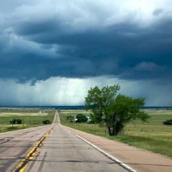 Road passing through landscape against storm clouds