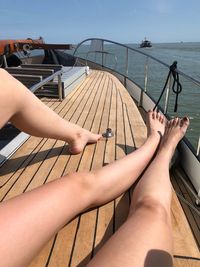 Low section of woman relaxing on railing by sea against sky