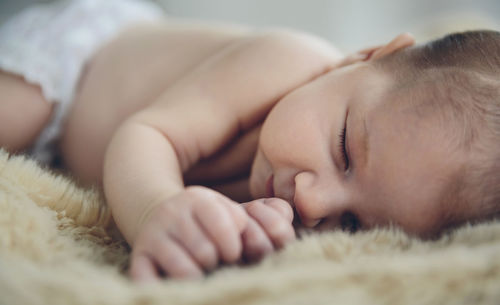 Close-up of shirtless baby girl sleeping on bed