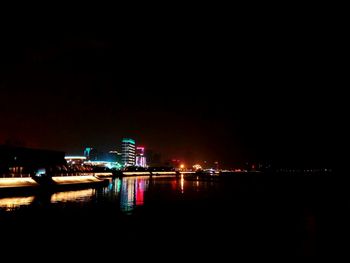 Illuminated city by river against clear sky at night