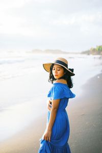 Woman wearing hat standing at beach against sky