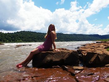 Woman standing on rock by sea against sky