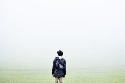 Rear view of man standing on field against sky in foggy weather