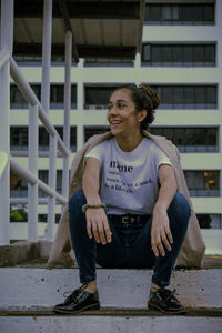 Young woman looking away while sitting on staircase in city