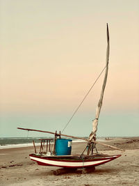 Fishing boat moored on beach against sky during sunset