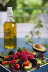 Salad with red berries, cherry tomatoes and avocado, on a blue table.