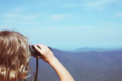 Rear view of woman looking through binoculars against sky