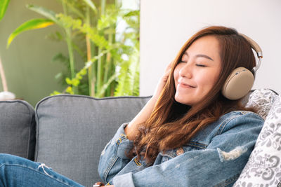 Smiling young woman listening music while sitting on sofa