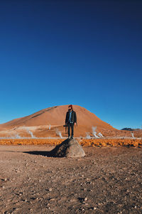 Full length of man standing on desert against clear blue sky