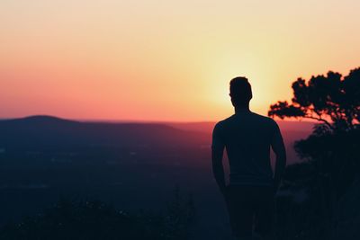 Rear view of man looking at mountain view against sky during sunset