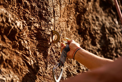 Cropped hand of female hiker attaching carabiner on hook over rocky cliff