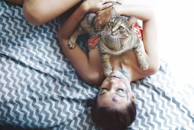 Woman lying with cat on bed at home