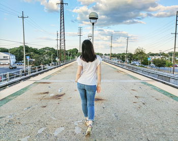 Rear view of woman walking on bridge against cloudy sky