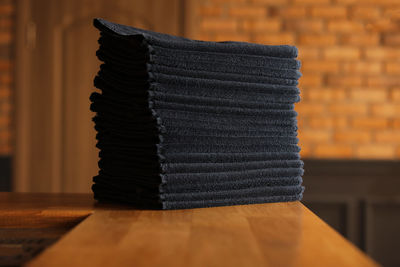 Stacked black bathroom towels on a wooden table and brick wall background. spa salon, barbershop.