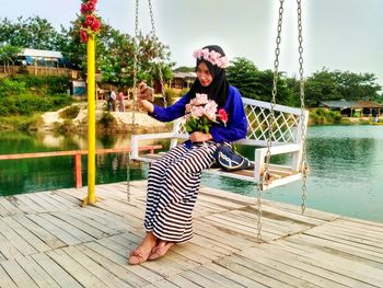Woman sitting with bouquet on swing against lake