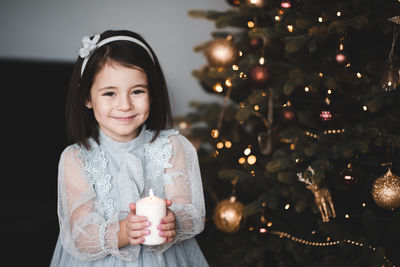 Portrait of cute girl holding candle sitting on sofa by illuminated christmas tree